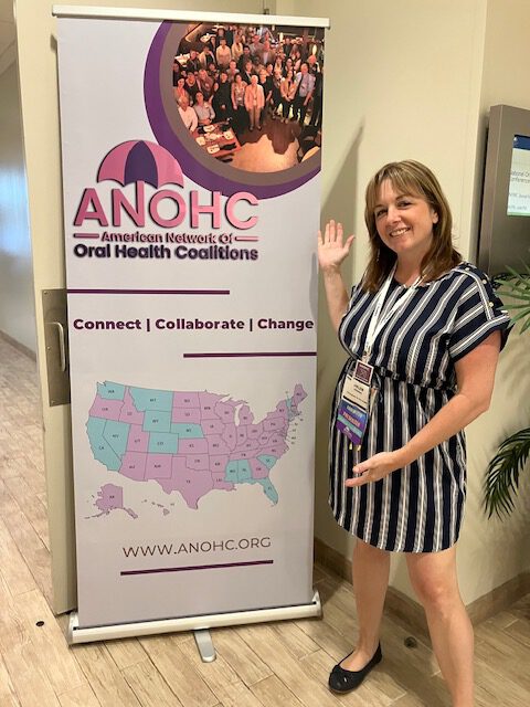 A coalition member waves beside an ANOHC banner featuring the U.S. coalition map at a conference.